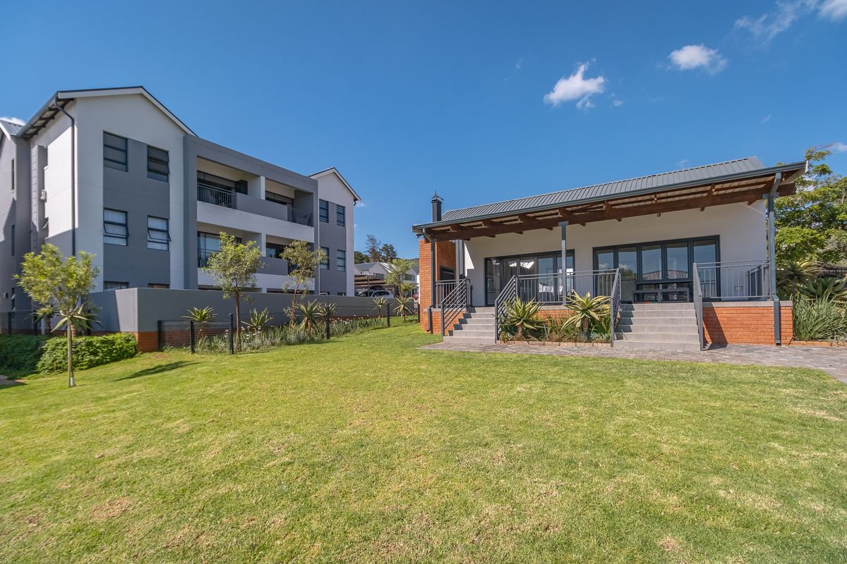 A well-maintained rear exterior view of the apartment complex featuring a covered patio, brick accents, and a spacious landscaped garden area.