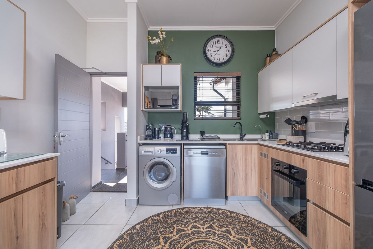 Modern kitchen featuring wood-tone and white cabinetry, gas hob, built-in oven, integrated dishwasher, and tiled finishes with a vibrant green accent wall.