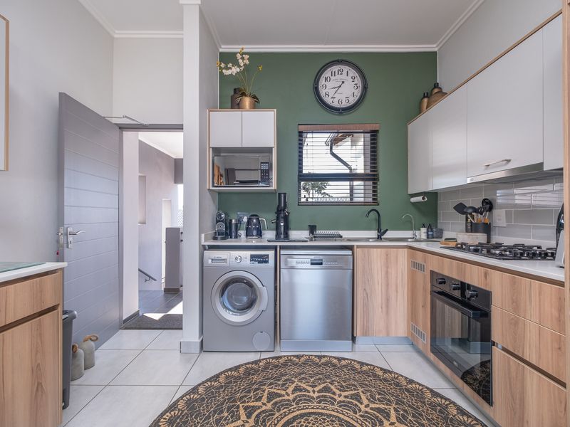 Modern kitchen featuring wood-tone and white cabinetry, gas hob, built-in oven, integrated dishwasher, and tiled finishes with a vibrant green accent wall.
