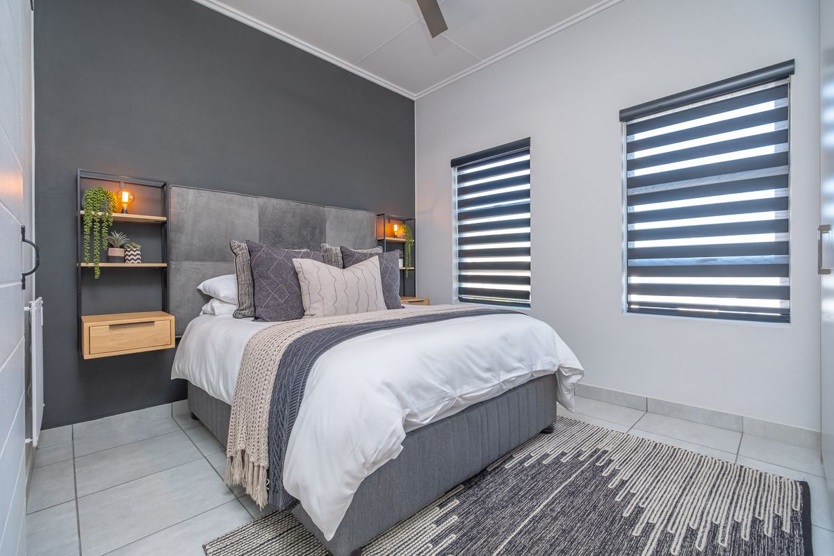A modern, well-maintained bedroom featuring tiled flooring, a dark accent wall, built-in shelving, and dual roller blinds for light control.