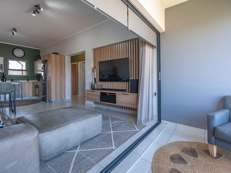 Modern open-plan living area featuring a stylish slatted timber media wall, tiled floors, and seamless transition to an outdoor space through large sliding glass doors.