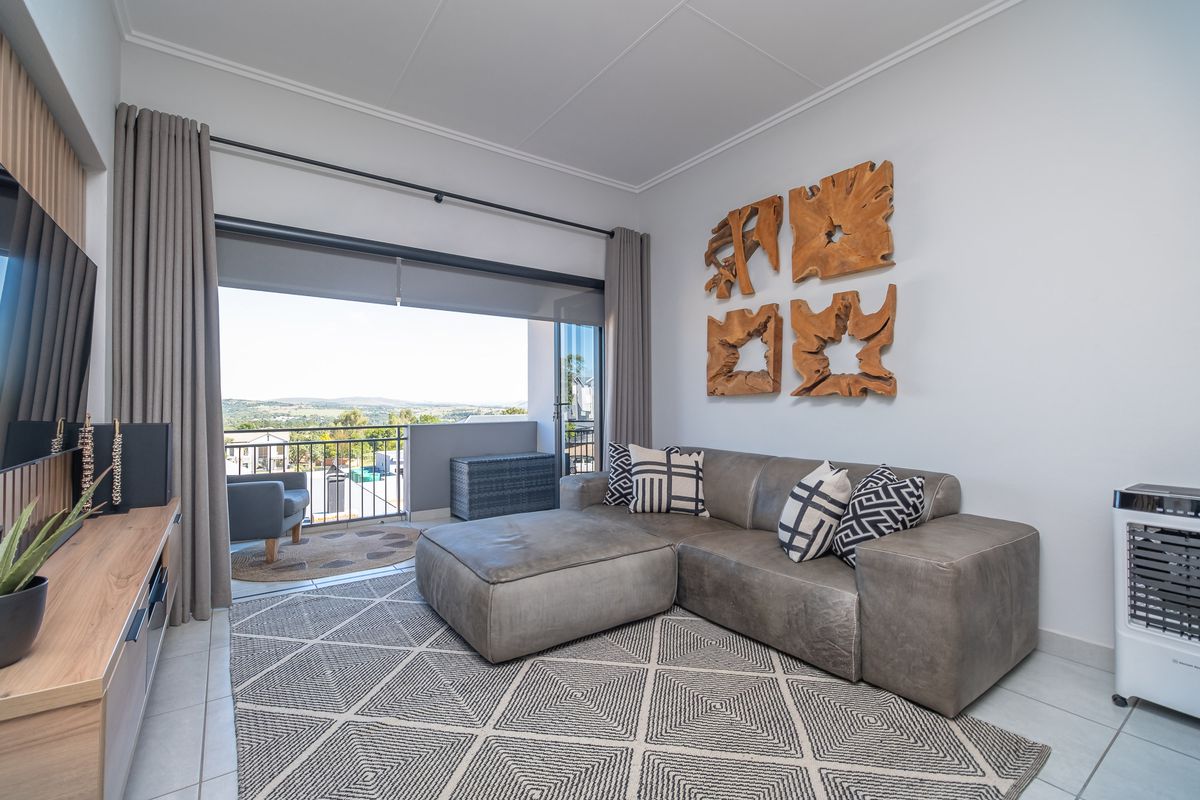 A bright and modern living room featuring tiled floors and large sliding glass doors that open onto a balcony with scenic views.