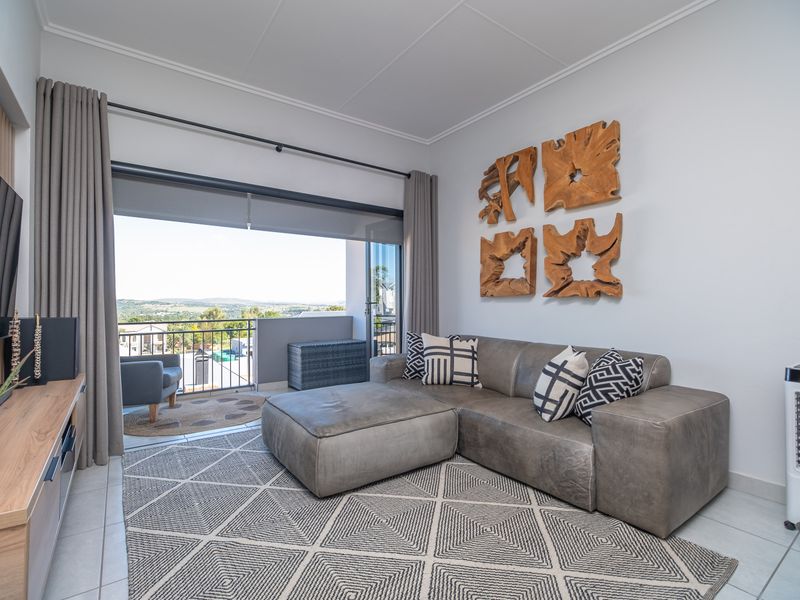 A bright and modern living room featuring tiled floors and large sliding glass doors that open onto a balcony with scenic views.