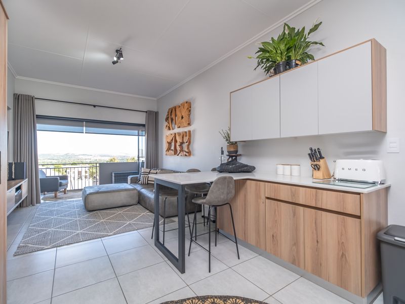 Modern open-plan living area featuring a sleek kitchen with wood-finish cabinetry, stone countertops, and seamless access to a private balcony with scenic views.