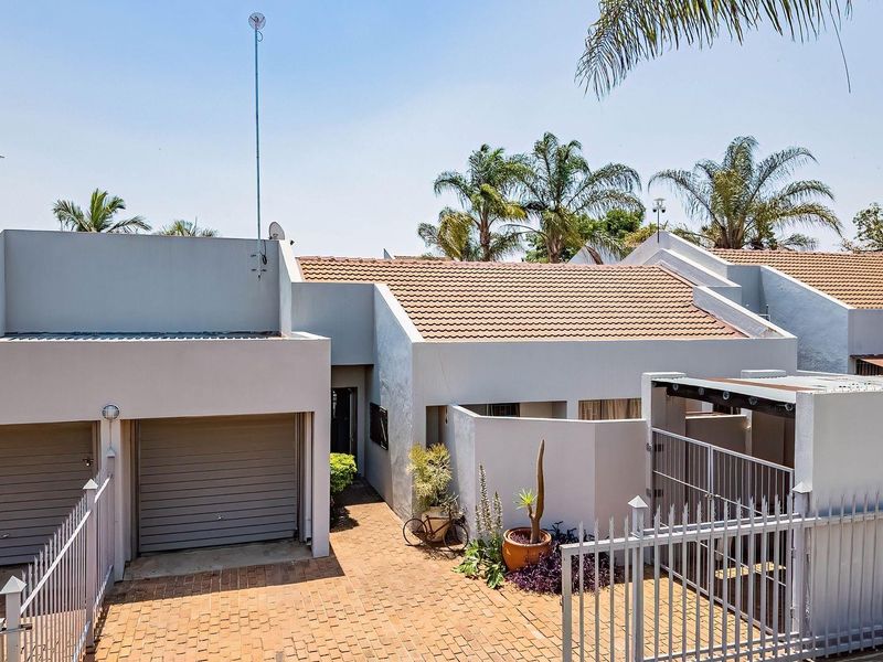 Front elevation of a townhouse featuring a double garage, paved driveway, and secure gated entrance with a tiled roof.
