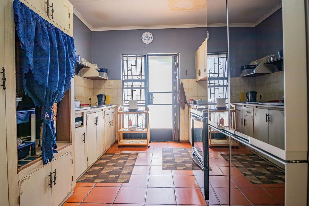 A functional kitchen featuring tiled flooring, built-in cabinetry, and a tiled backsplash, with a security gate leading to the exterior.