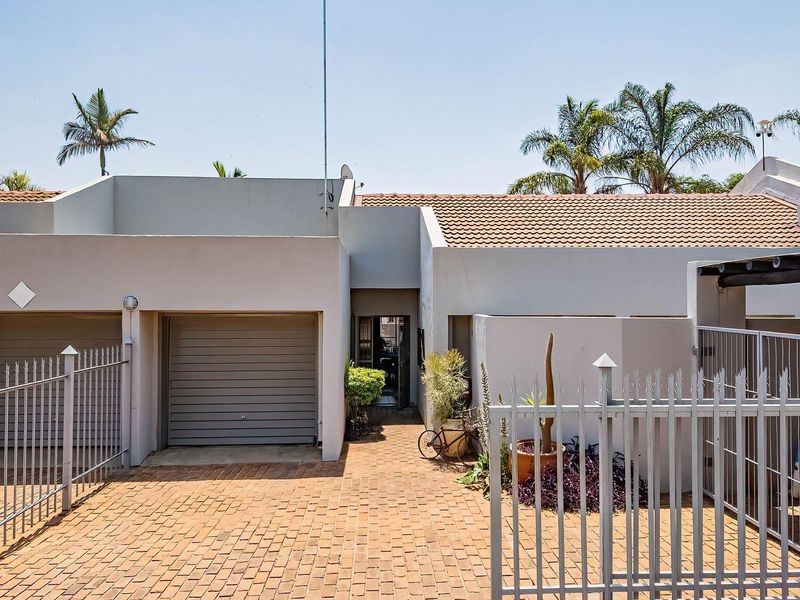 Front exterior view of a townhouse featuring a double garage, brick paved driveway, and secure metal fencing.