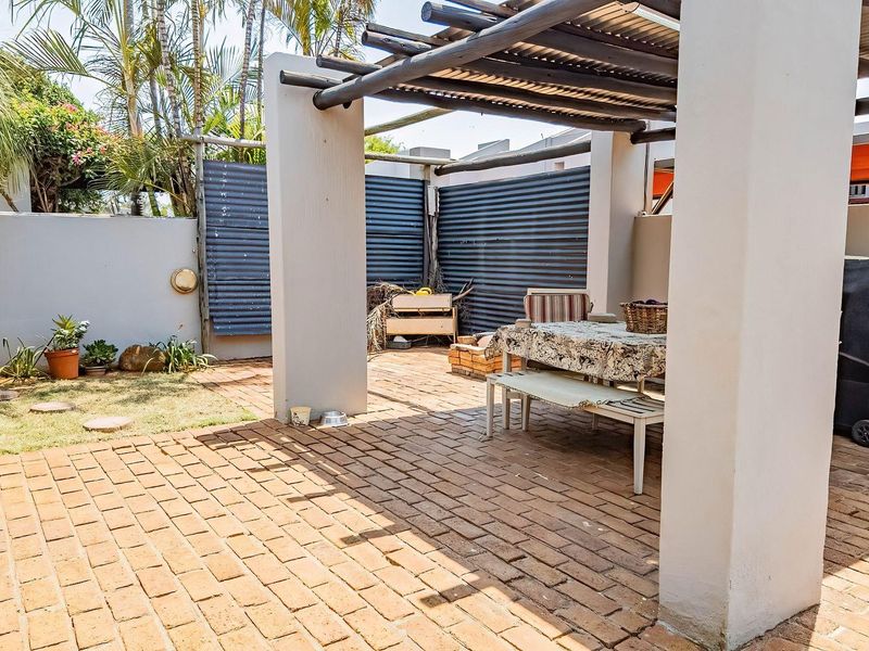 Covered outdoor patio area featuring brick paving, a timber pergola structure, and corrugated metal privacy screening, providing a functional space for outdoor dining.