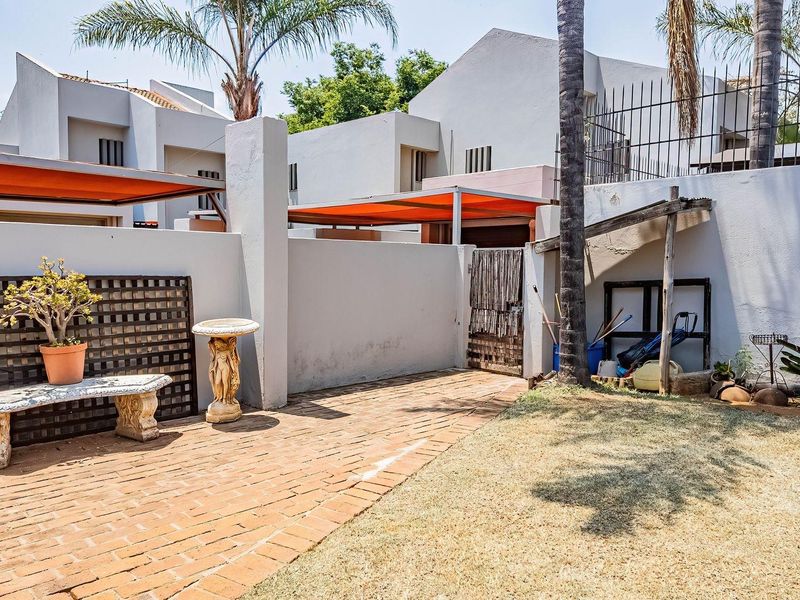 A private rear courtyard featuring brick paving, a retractable awning for shade, and a secure boundary wall with metal fencing.