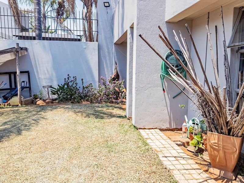 A private rear garden area featuring a paved walkway, boundary wall with security spikes, and a small lawn space.