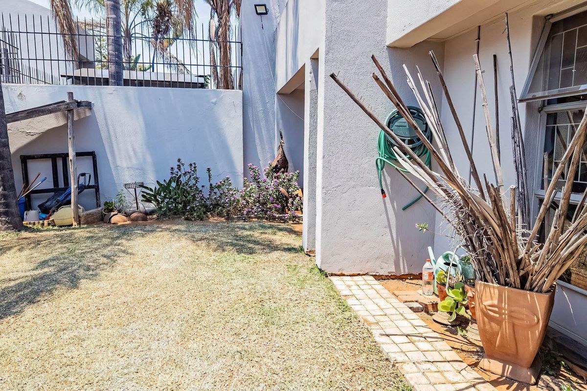 A private rear garden area featuring a paved walkway, boundary wall with security spikes, and a small lawn space.