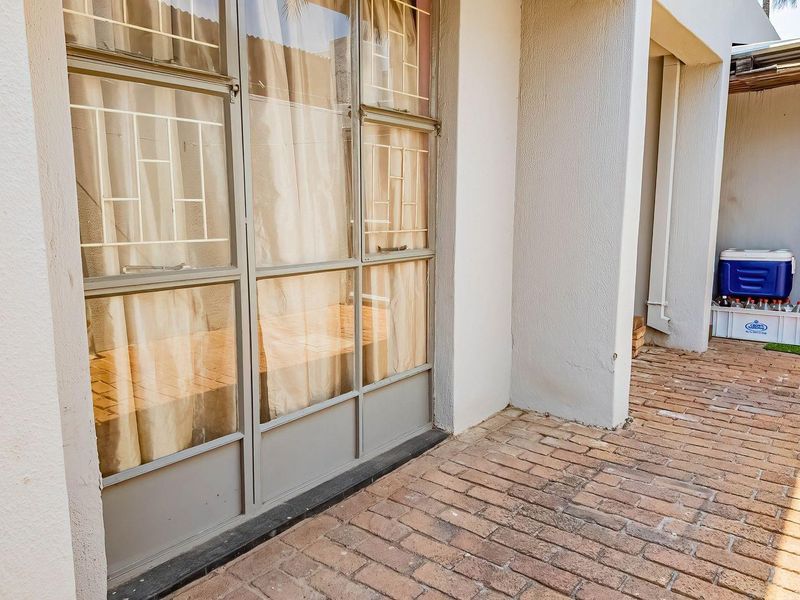 A paved outdoor patio area featuring steel-framed glass doors and a functional drainage downpipe, providing a simple transition to the exterior space.