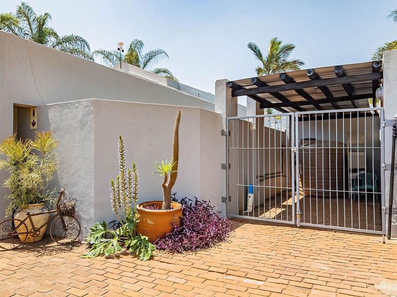 Front exterior view of the townhouse featuring brick paving, a secure metal gate, and a covered pergola area with a water storage tank.