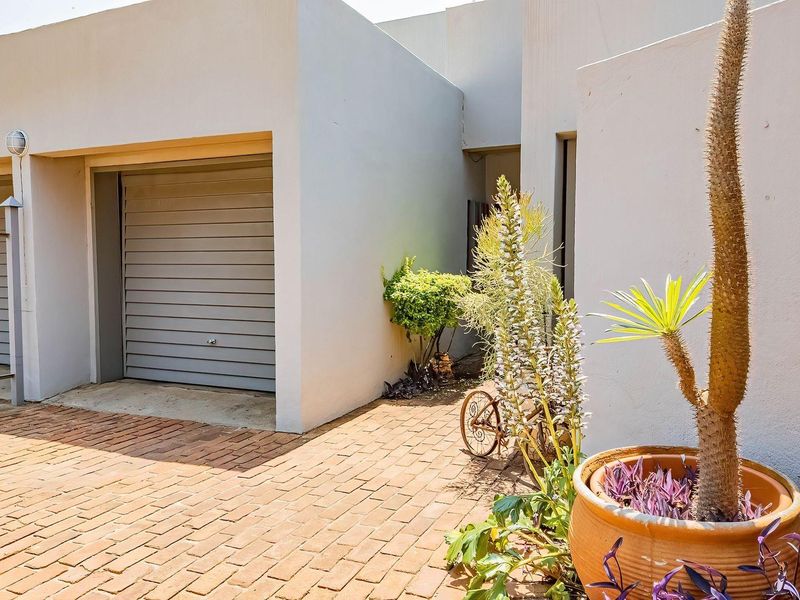 Front exterior view of the townhouse featuring a garage, brick paved driveway, and secure metal fencing.