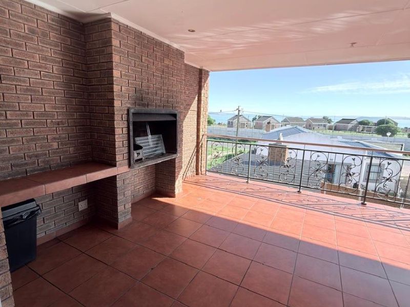 A spacious covered balcony featuring a built-in braai, tiled flooring, and a wrought iron balustrade, offering an elevated outdoor entertainment area with scenic views.