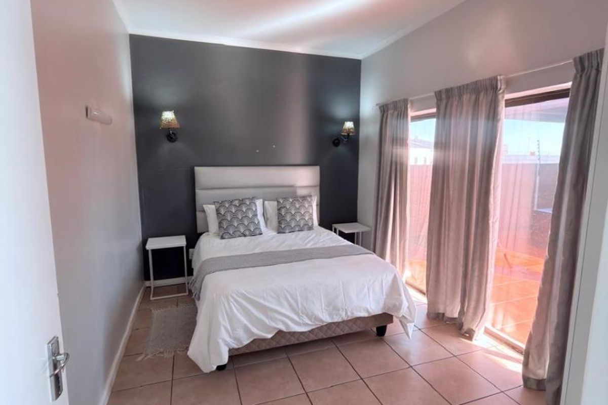 A well-lit bedroom featuring tiled flooring, a dark accent wall, and a sliding glass door providing direct access to the outdoor area.