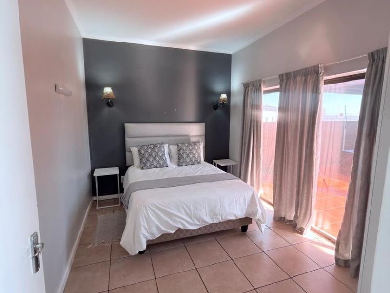 A well-lit bedroom featuring tiled flooring, a dark accent wall, and a sliding glass door providing direct access to the outdoor area.