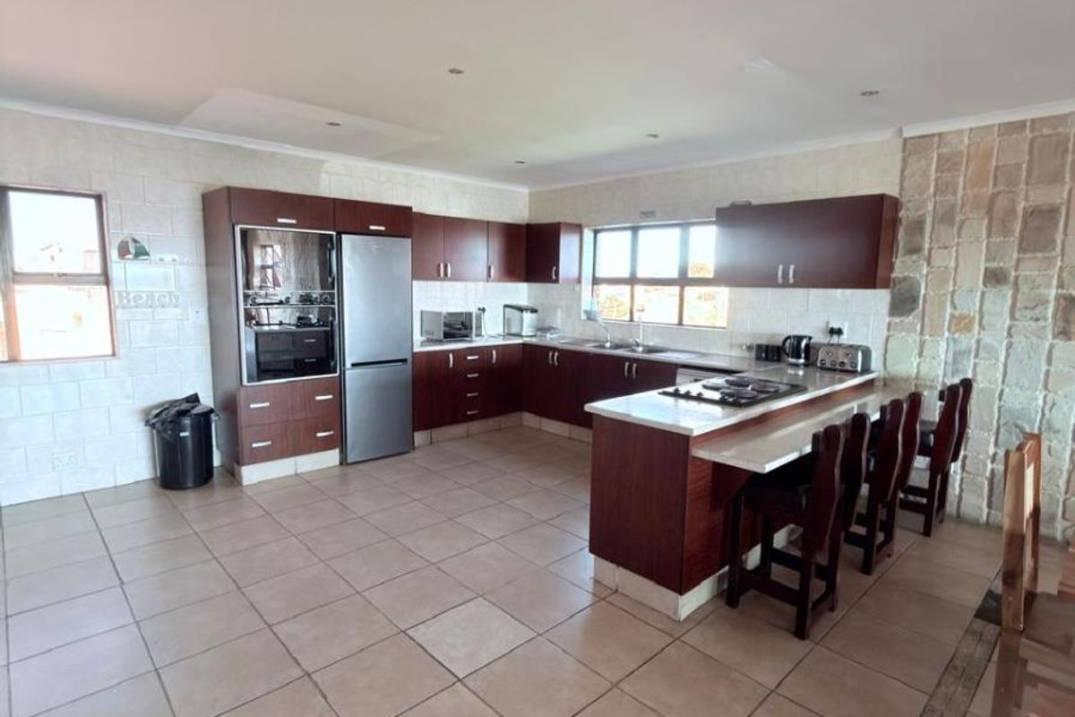 Spacious kitchen featuring dark wood cabinetry, a breakfast bar with integrated hob, stone feature wall, and tiled flooring.