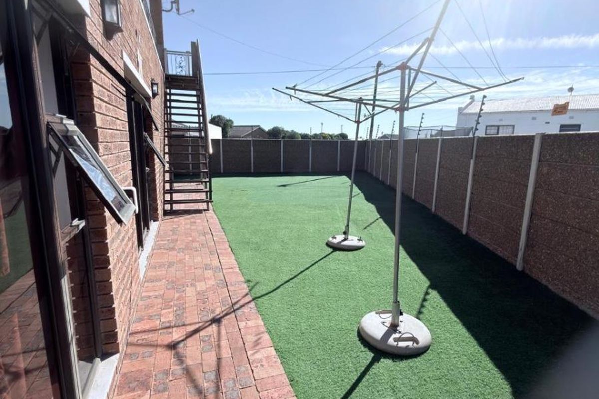 Rear exterior area featuring brick paving, artificial lawn, and a secure boundary wall with access via an external metal staircase.