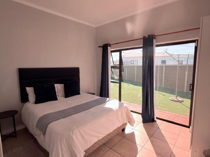 A bright bedroom featuring tiled flooring and a large sliding glass door providing direct access to the rear garden area.