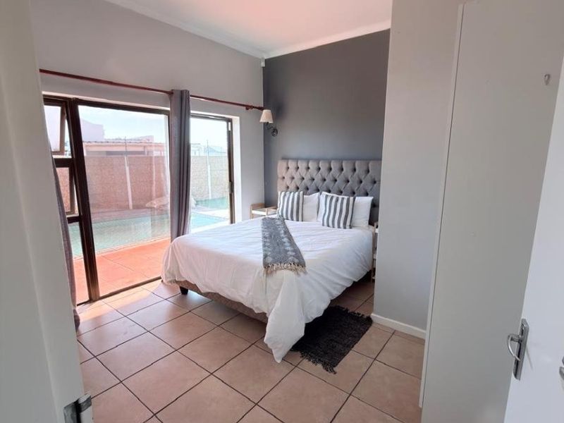 A well-lit bedroom featuring tiled flooring, a dark accent wall, and a sliding glass door providing direct access to the pool area.