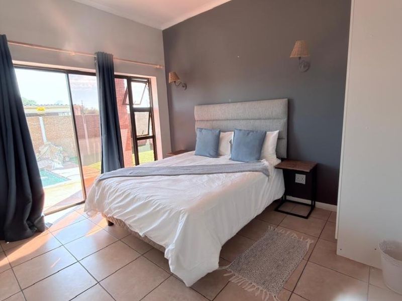 A well-lit bedroom featuring tiled flooring, a built-in wardrobe, and a sliding glass door providing direct access to the outdoor pool area.