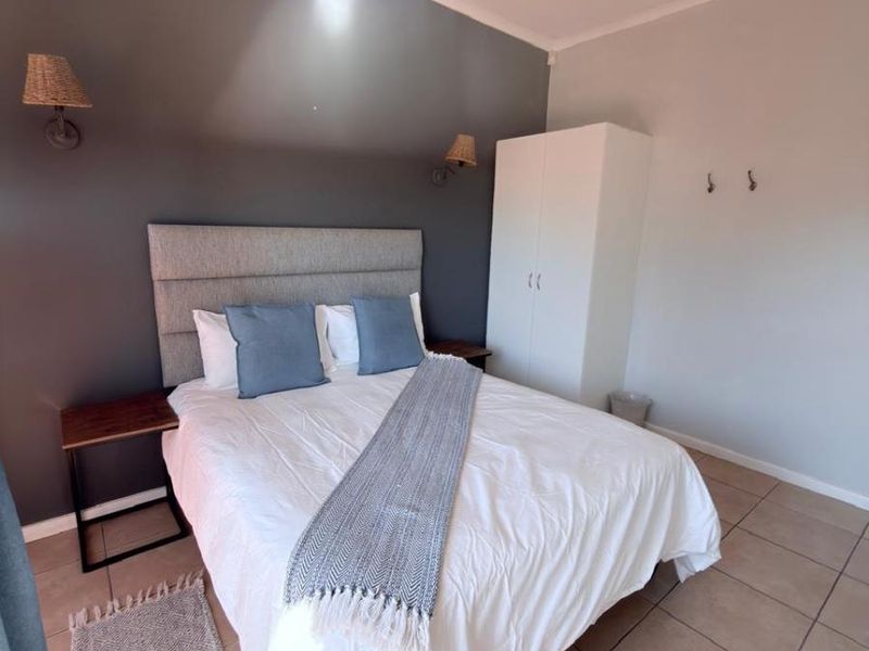 A well-maintained bedroom featuring tiled flooring, a built-in wardrobe, and modern wall-mounted lighting, creating a clean and functional living space.