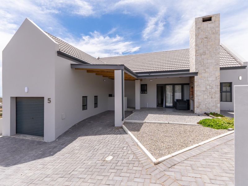 Modern front elevation featuring a paved driveway, integrated garage, covered patio area, and a distinctive stone-clad chimney.