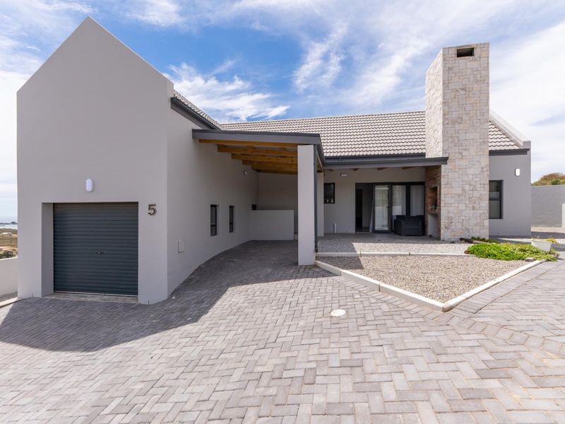 Modern single-story residence featuring a paved driveway, integrated garage, covered carport, and a prominent stone chimney with an outdoor fireplace.