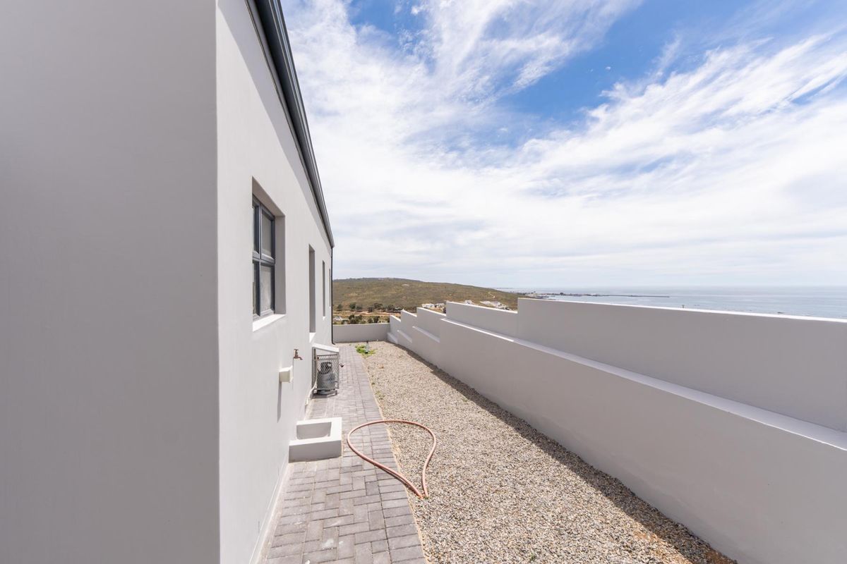 A clean rear exterior area featuring a paved walkway, gravel landscaping, and a modern retaining wall with scenic coastal views.
