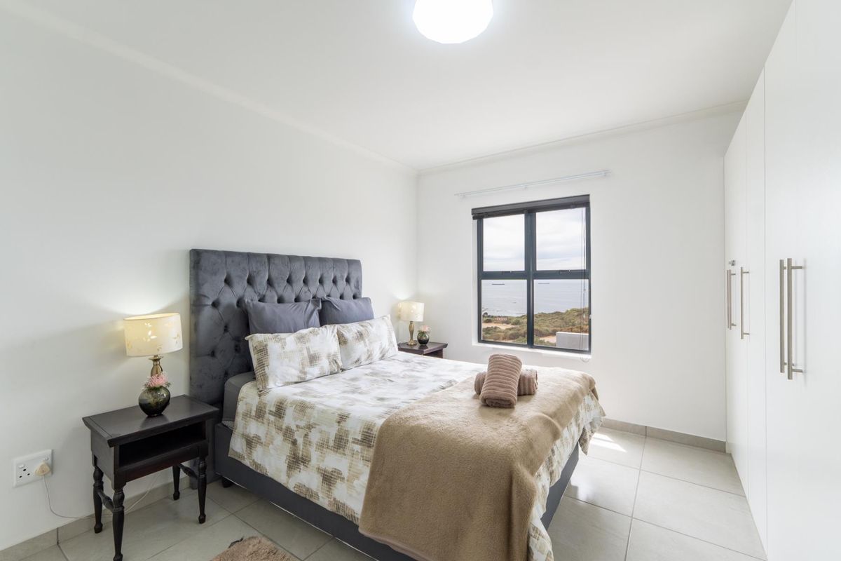 A bright bedroom featuring tiled flooring, built-in cupboards, and a window offering scenic coastal views.