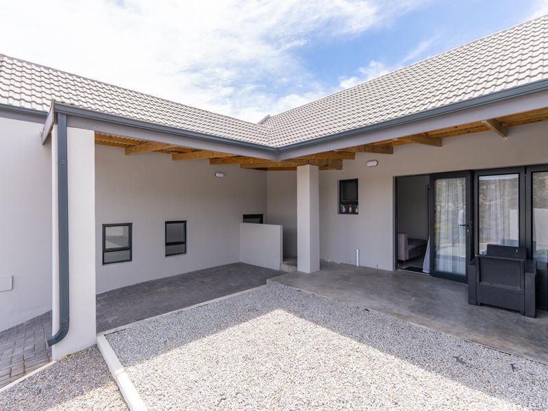 A covered patio area featuring exposed timber rafters, concrete flooring, and sliding glass door access to the interior.