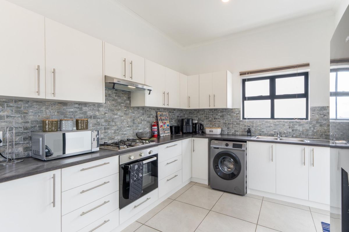 Modern kitchen featuring white cabinetry, stone tile backsplash, gas hob, built-in oven, and integrated laundry appliance space with tiled flooring.