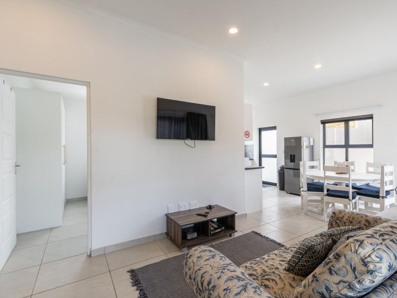 An open-plan living and dining area featuring neutral tiled flooring, recessed lighting, and a seamless flow between the lounge and kitchen space.