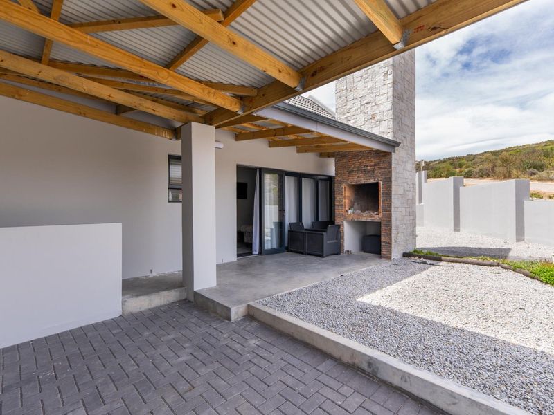 Covered outdoor patio featuring a built-in braai with stone cladding, timber roof beams, and paved flooring, providing a seamless transition to the garden area.