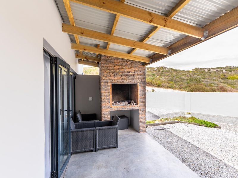 Covered patio area featuring a built-in stone-clad braai, concrete flooring, and modern stacking doors leading to the outdoor space.