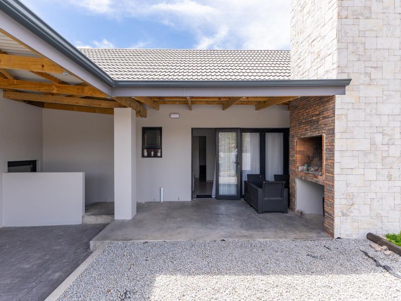 Covered outdoor patio featuring a built-in braai, stone cladding, and exposed timber rafters, providing a seamless transition to the interior living space.