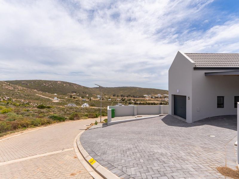 Modern front elevation featuring a paved driveway, single garage, and boundary wall, set against a scenic landscape.