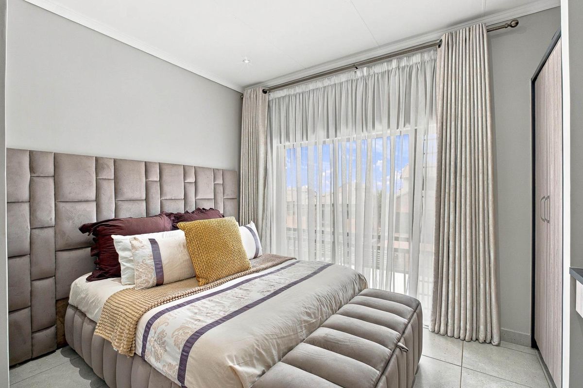 A well-maintained bedroom featuring tiled flooring, a coved ceiling, and a large sliding glass door with floor-to-ceiling curtains providing natural light.