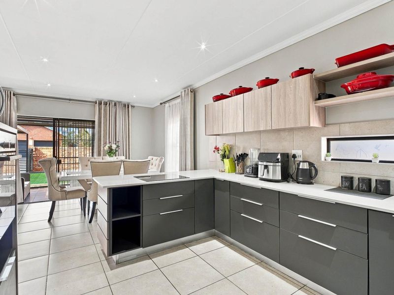 Modern open-plan kitchen and dining area featuring sleek dark cabinetry, stone countertops, integrated appliances, and direct access to an outdoor patio through sliding doors.