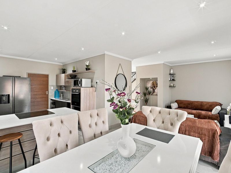 Modern open-plan living area featuring a contemporary kitchen with a central island, built-in oven, and sleek cabinetry, seamlessly flowing into the dining and lounge space.