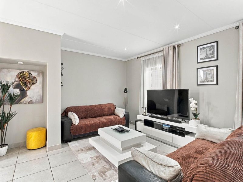 A well-maintained living room featuring neutral wall tones, tiled flooring, and recessed ceiling lighting, creating a bright and comfortable atmosphere.