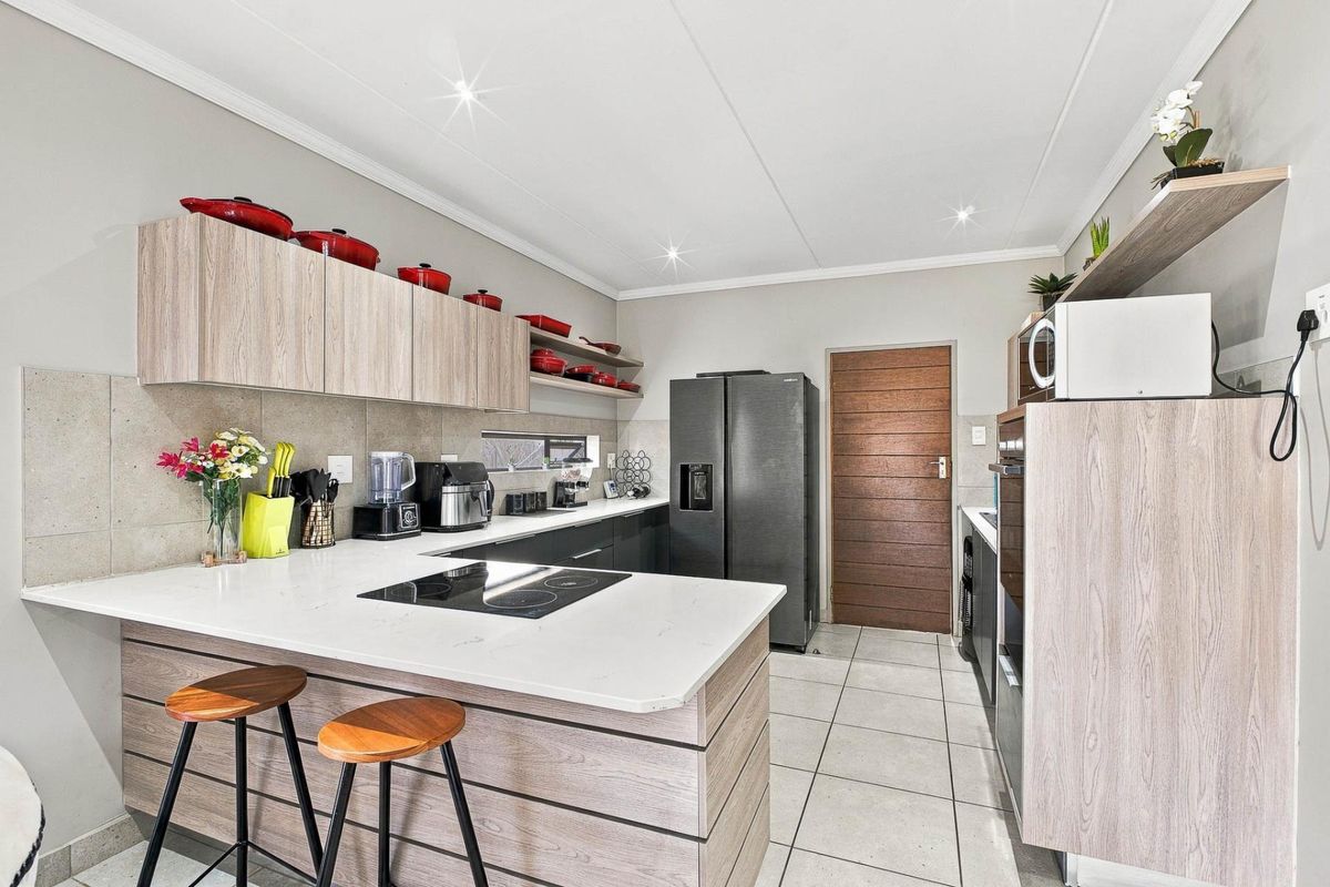 Modern kitchen featuring light wood-tone cabinetry, stone countertops, an integrated electric cooktop, and tiled flooring with a clean, contemporary finish.