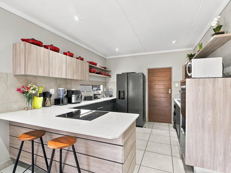 Modern kitchen featuring light wood-tone cabinetry, stone countertops, an integrated electric cooktop, and tiled flooring with a clean, contemporary finish.