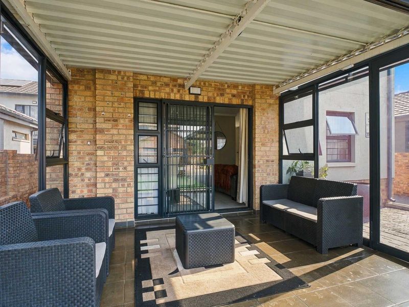 A covered patio area featuring brick walls, tiled flooring, and aluminium-framed windows, providing a functional outdoor living space.