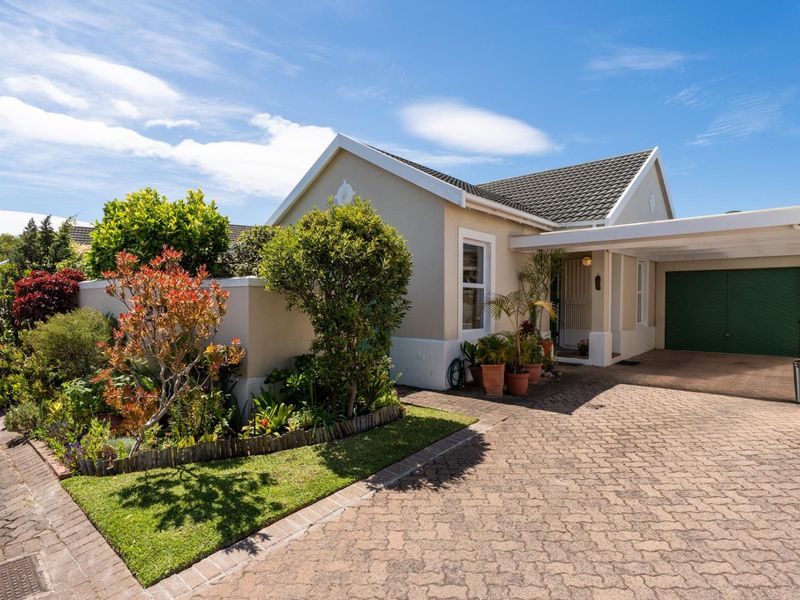 A well-maintained front exterior featuring a paved driveway, integrated carport, garage, and established garden with a boundary wall.