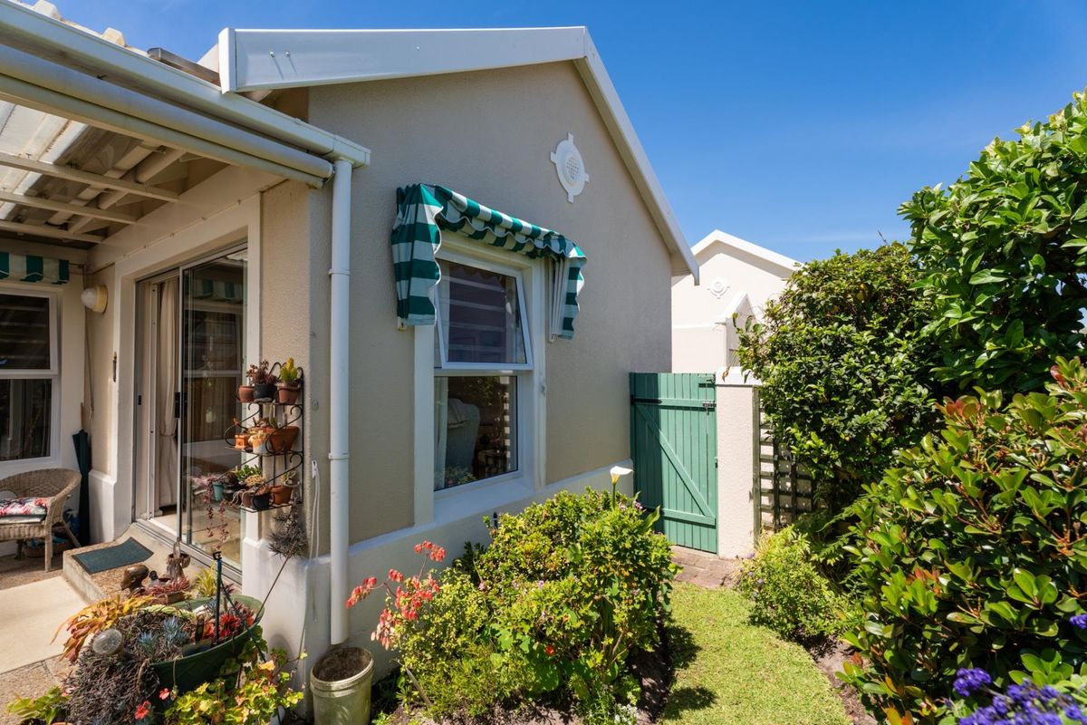 Rear exterior view of the property featuring a paved patio area, sliding glass doors, and a private side gate with established garden landscaping.
