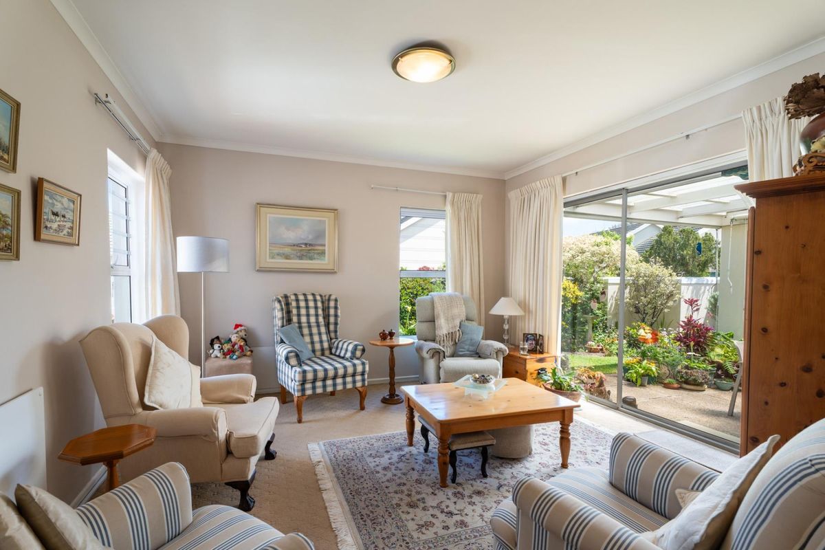 A comfortable living room featuring carpet flooring, neutral walls, and large sliding glass doors that provide direct access to a covered patio and garden.