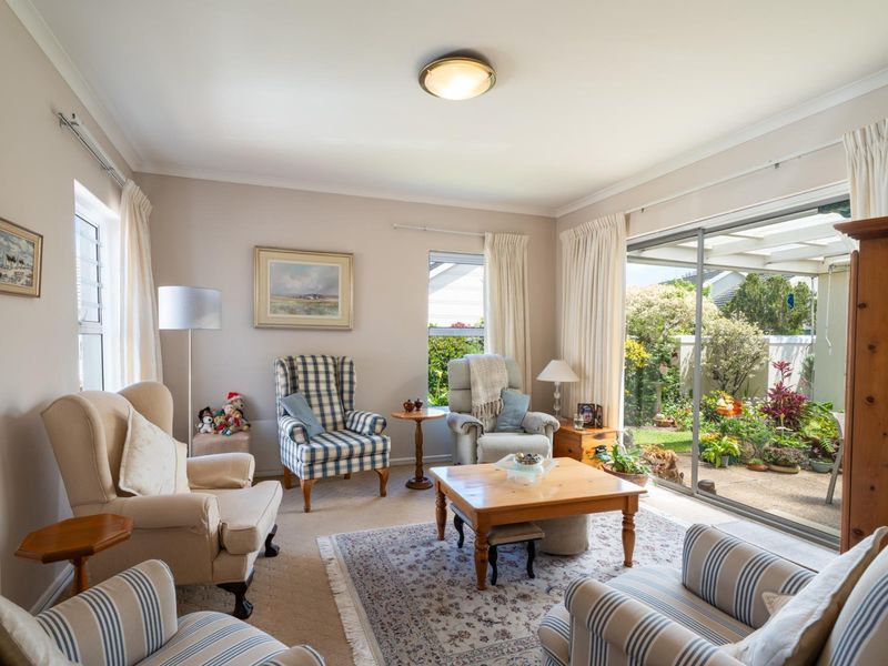 A comfortable living room featuring carpet flooring, neutral walls, and large sliding glass doors that provide direct access to a covered patio and garden.