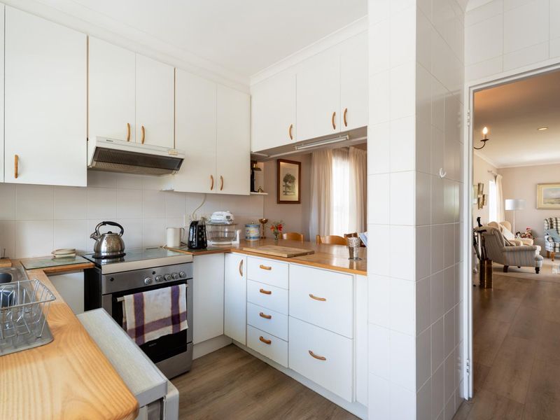 A functional kitchen featuring white cabinetry, timber countertops, and a stainless steel stove, with a convenient pass-through window overlooking the adjacent living area.